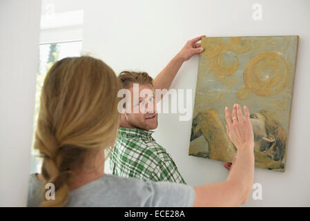 Woman helping man hanging painting wall Stock Photo