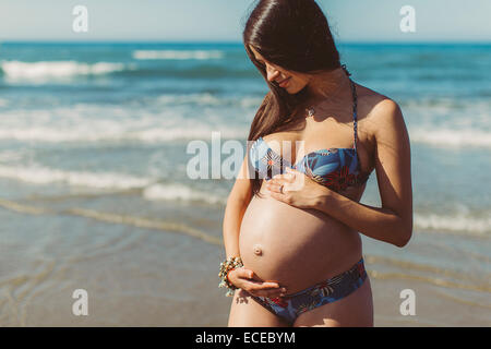 Young pregnant woman standing on beach Stock Photo