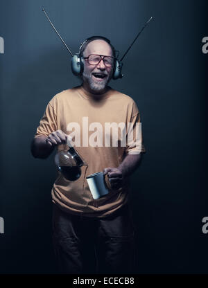 Senior man wearing headphones, singing and pouring tea Stock Photo