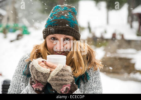 Woman standing in snow holding a cup of tea Stock Photo