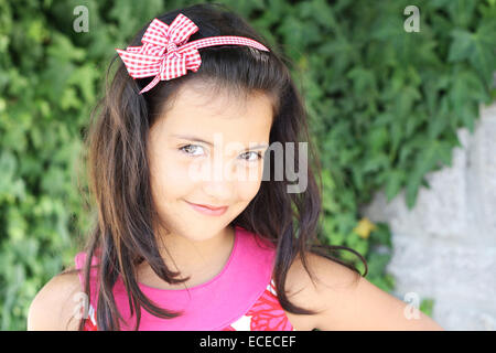 Sweet smiling little girl (6-7) with long dark hair on green ivy background Stock Photo