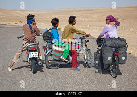 Iranian boys on motorbikes talking to female Western touring cyclist in Iran, close to the Turkmenistan border in Karakum desert Stock Photo