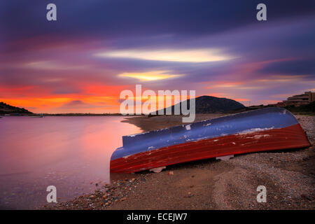Lonely fishing boat left at shore against a spectacular and colorful sunset with colored clouds passing over the boat Stock Photo