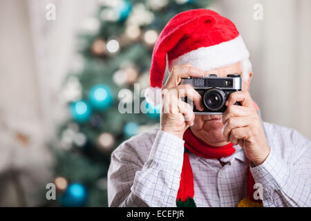 Senior man in Santa's hat taking photo on Christmas background Stock Photo