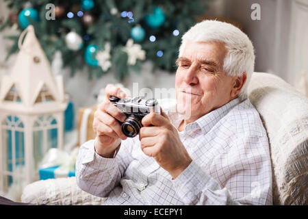 Senior man looking at display of retro style camera and smiling against Christmas background Stock Photo