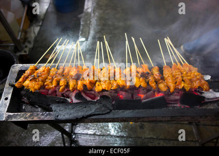 Spicy chicken satay sticks grilling over a charcoal BBQ grill in Asia Stock Photo