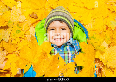 Happy little four years old boy laying in the yellow autumn leaves, smiling and covered with some of them Stock Photo