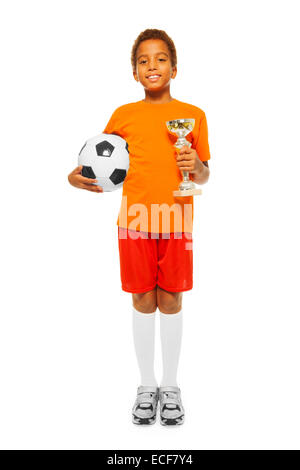 Happy African black boy with curly short hair holding soccer ball and winners prize cup wearing sport team uniform standing isol Stock Photo