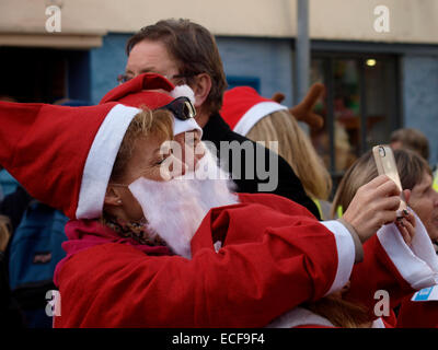 Older couple dressed as Santa taking a selfie before the start of the Charity Santa run at the Padstow Christmas festival, Co Stock Photo