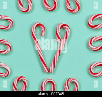 Image of red and white stripped candy canes on a solid light green background. Pattern of a heart shape in center of frame with Stock Photo