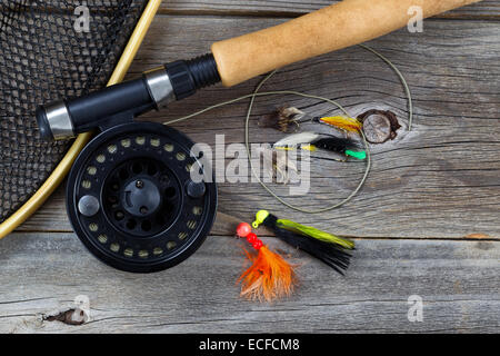 Close up top view of a fishing fly reel, with line, landing net and assorted flies, and partial cork handled pole on rustic wood Stock Photo