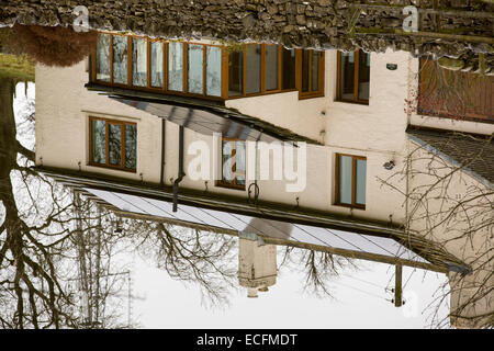 Solar panels on a house roof reflected in the Leeds Liverpool canal near Skipton, UK.