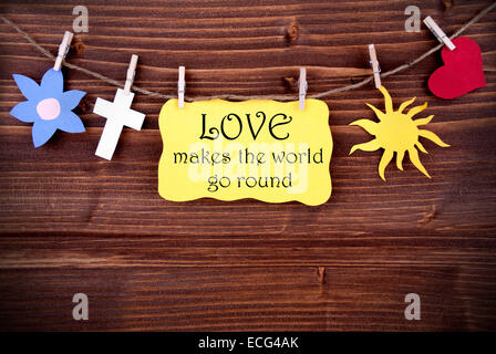 Yellow Tag Or Label With Heart And Flower And Cross And Sun On A Line With Life Quote Love Makes The World Go Round On Wooden Ba Stock Photo