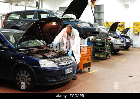 Mechanic in repair garage checking car's engine covering car with a tarpaulin Stock Photo