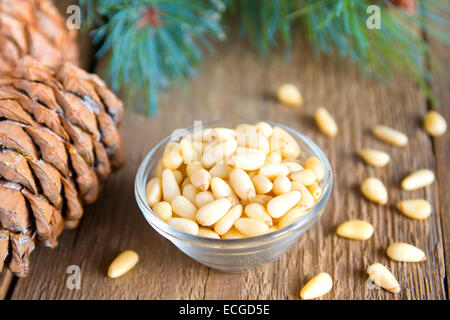 Pine nuts in bowl with cones close up on rustic wooden background, horizontal Stock Photo
