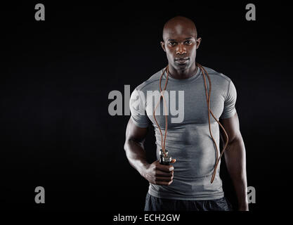 Handsome muscular man with jumping rope on black background. Fit African model with lots of copy space. Stock Photo