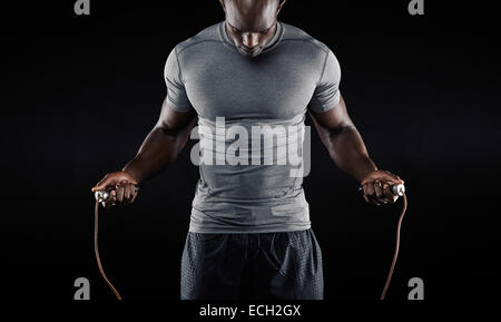 Muscular man skipping rope. Portrait of muscular young man exercising with jumping rope on black background Stock Photo