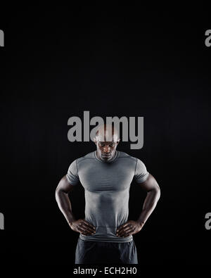 Portrait of muscular young man in sportswear staring at camera against black background. African athlete with his hands on hips Stock Photo