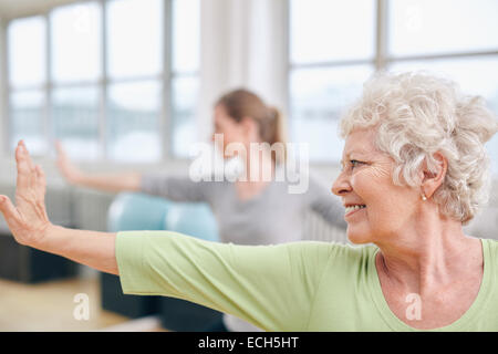 Close-up shot of elderly woman doing stretching workout at yoga class. Women practicing yoga at health club. Stock Photo