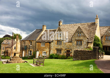 A village green with a bench and a row of Cotswold stone cottages and an inky-black sky. Stock Photo