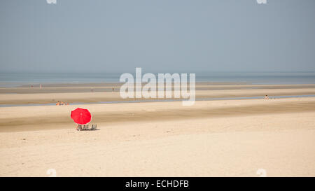 A deserted French beach with one person sunbathing beneath a red parasol or umbrella Stock Photo