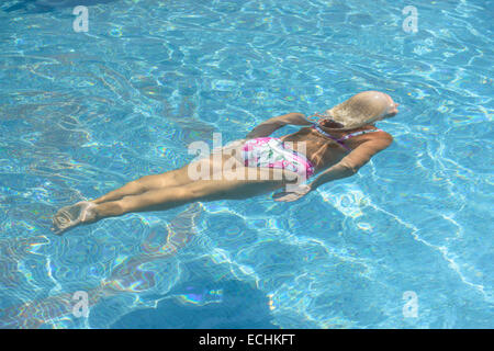 High angle view of aged woman that is swimming underwater in bright blue water of pool. Stock Photo