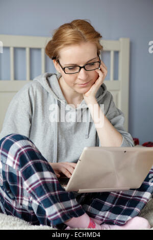 Young woman working on her laptop on the bed Stock Photo