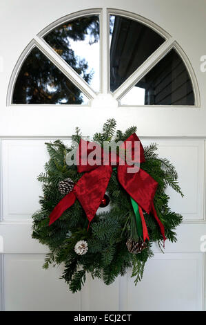 Homemade traditional green and red Christmas wreath hanging on the white front door of a house Stock Photo