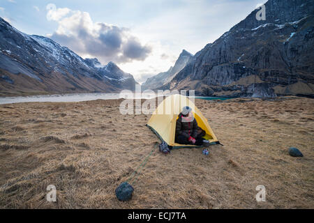 Female backpacker takes in view from tent while camping at Horseid beach, Moskenesøy, Lofoten Islands, Norway Stock Photo