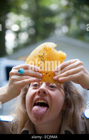 A young woman eats fresh honey as she squeezes it out of a honeycomb. Stock Photo