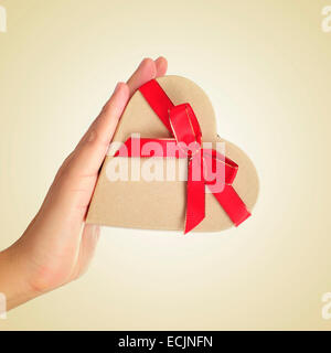 a heart-shaped gift box tied with a red ribbon in the hand of a man Stock Photo