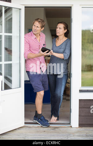 Full length of couple looking away while using digital tablet at doorway Stock Photo
