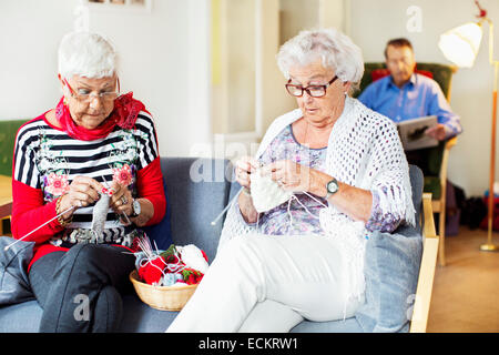 Senior women knitting while man reading book in background at nursing home Stock Photo