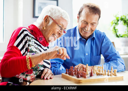 Happy senior couple playing chess at table in nursing home Stock Photo