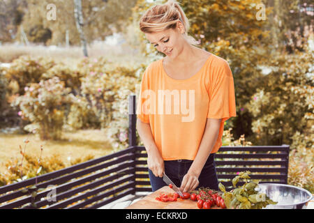 Happy young woman slicing tomatoes on cutting board at yard Stock Photo