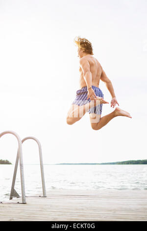 Full length rear view of man diving into lake against clear sky Stock Photo
