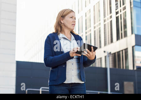 Businesswoman looking away while using digital tablet outside office building Stock Photo