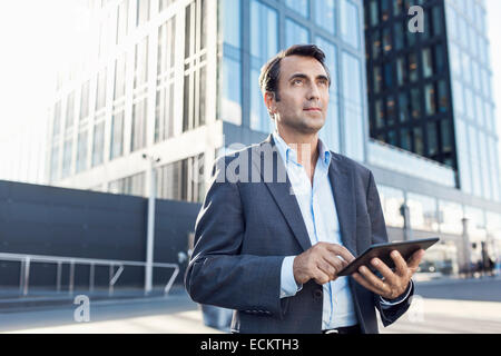 Confident businessman looking away while using digital tablet outside office building Stock Photo