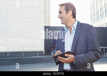 Smiling businessman looking away while using digital tablet outside office building Stock Photo