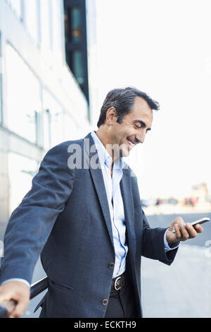 Happy businessman using mobile phone on sidewalk Stock Photo