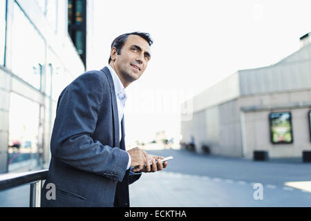 Confident businessman looking away while using mobile phone on sidewalk Stock Photo