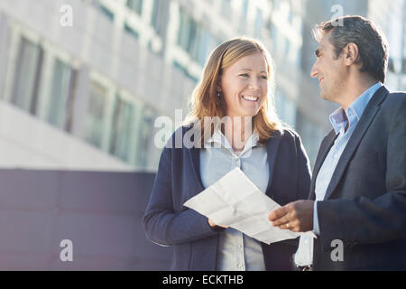 Smiling businesspeople discussing over document outside office building Stock Photo