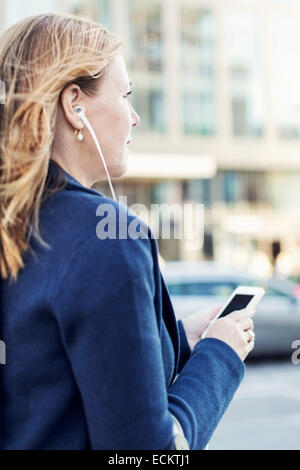 Businesswoman listening to music through headphones using mobile phone on street Stock Photo