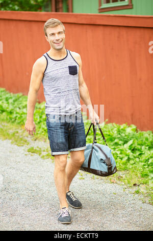 Full length portrait of smiling young man walking on street against house Stock Photo