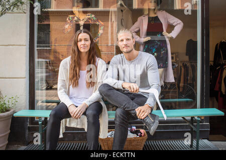 Portrait of owner with female worker sitting in front of clothing store Stock Photo