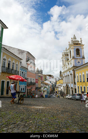 SALVADOR, BRAZIL - OCTOBER 15, 2013: A vendor walks in front of colorful buildings lining the cobblestone streets of Pelourinho. Stock Photo