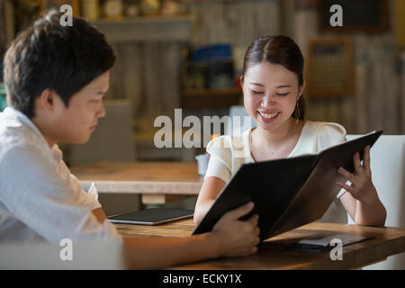 Woman and man sitting at a table in a cafe, looking at the menu, smiling. Stock Photo