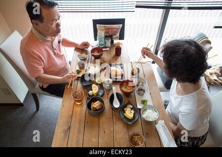 Woman and man sitting at a table, eating Japanese Food with chopsticks. Stock Photo