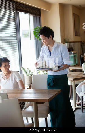 Waiter serving a woman seated at a table in a cafe. Stock Photo