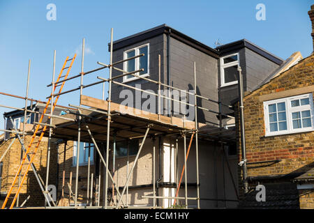 Scaffolding to a newly completed dormer / dormers / dormas / dorm roof extension with slate tile cladding on the roof on a Victorian terraced house in Twickenham. London. UK Stock Photo